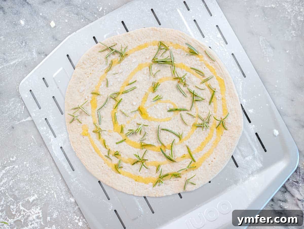 Perfect Ooni Pizza Dough Formula 38 Ooni pizza dough on a pizza peel with rosemary and olive oil
