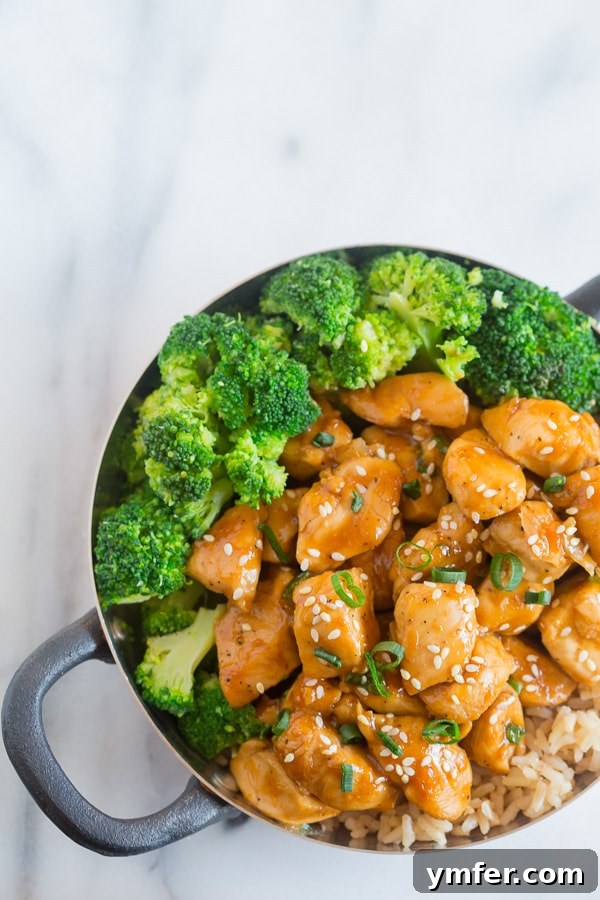 This 20 minute healthier orange chicken is the perfect weeknight dish. Close-up shot of Healthier Orange Chicken in a bowl, garnished with sesame seeds, emphasizing the rich sauce and tender chicken.