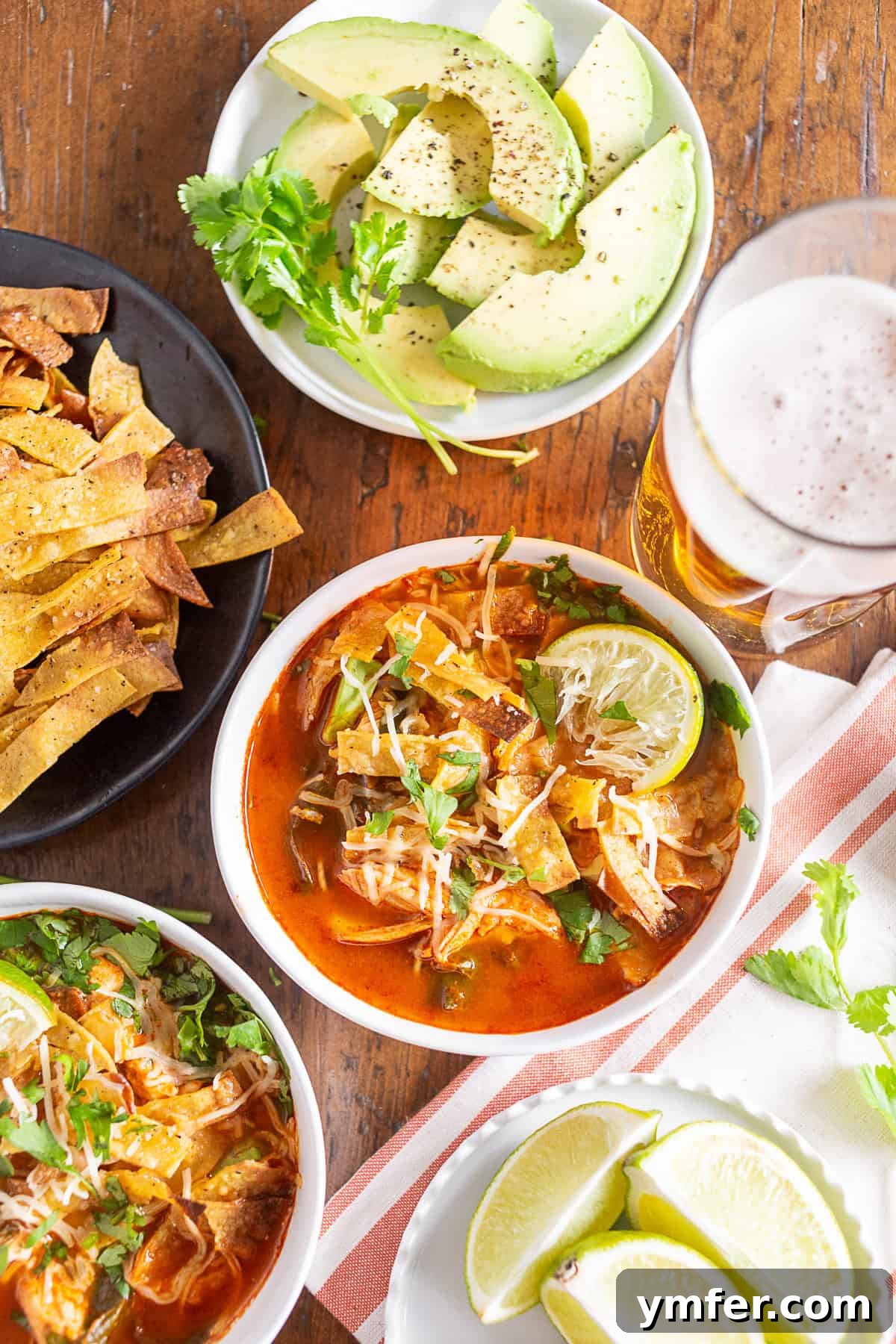 chicken and chard tortilla soup in a bowl surrounded by toppings and a beer
