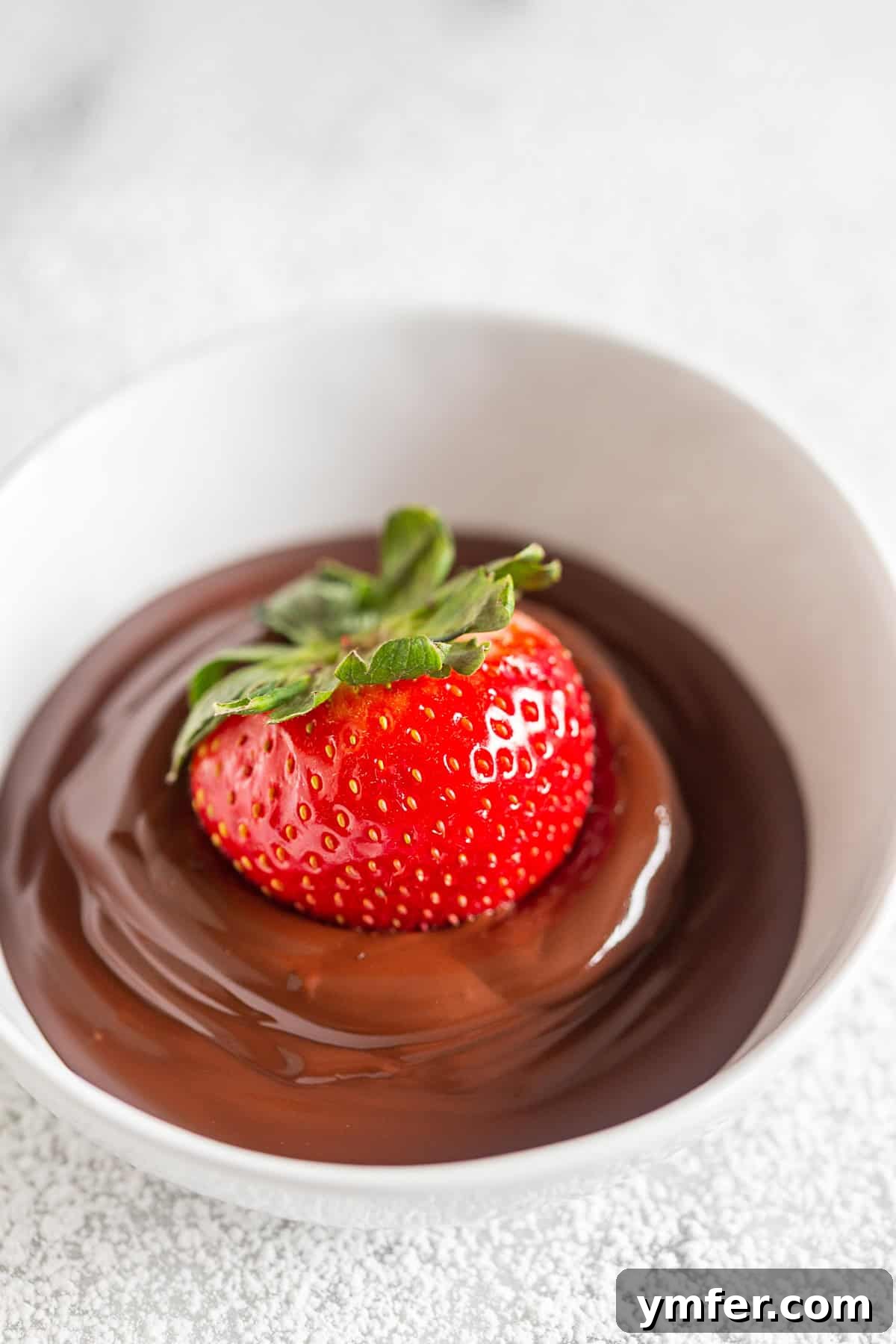 Berry Chocolate Bliss Waffles 3 A vibrant red strawberry is carefully submerged into a bowl of rich, melted dark chocolate, illustrating the decadent preparation process for the waffle topping.
