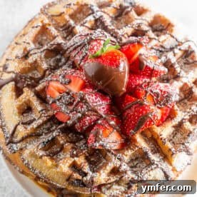 A vibrant and enticing close-up of a chocolate covered strawberry waffle, highlighting the fluffy texture and generous toppings.