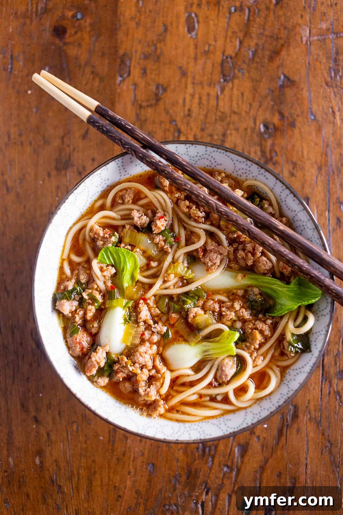 Blazing Pork Noodle Delight 2 A beautifully presented spicy pork noodle bowl in a rustic bowl with chopsticks, garnished with fresh herbs.