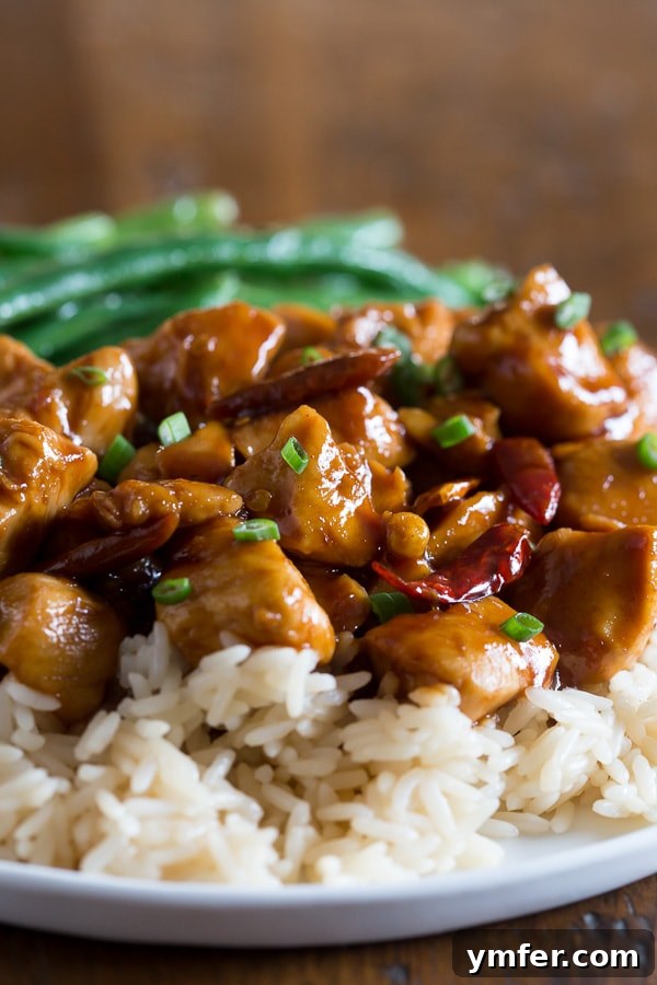 Lighter General Tso Chicken 3 A close-up of Healthier General Tso's Chicken served over a bed of fluffy white rice, adorned with thinly sliced green onions. The vibrant red-orange sauce glistens on the chicken, hinting at its perfect balance of sweet and spicy flavors, making it an enticing weeknight dinner.