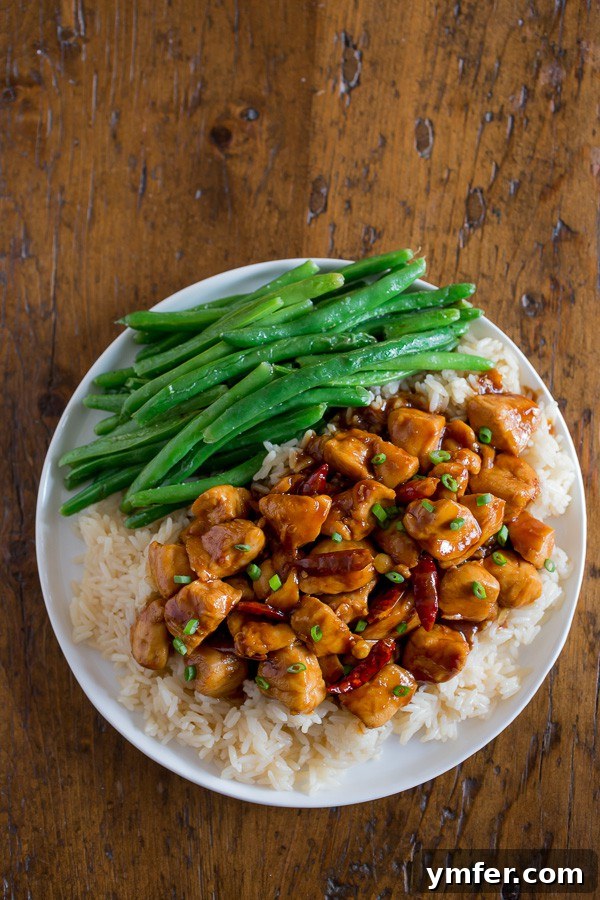 Lighter General Tso Chicken 4 A vibrant plate of Healthier General Tso's Chicken, served with a generous portion of white rice and a colorful medley of steamed vegetables like broccoli and carrots. The chicken is coated in a tantalizing, thick sauce, promising a wholesome and delightful meal experience.