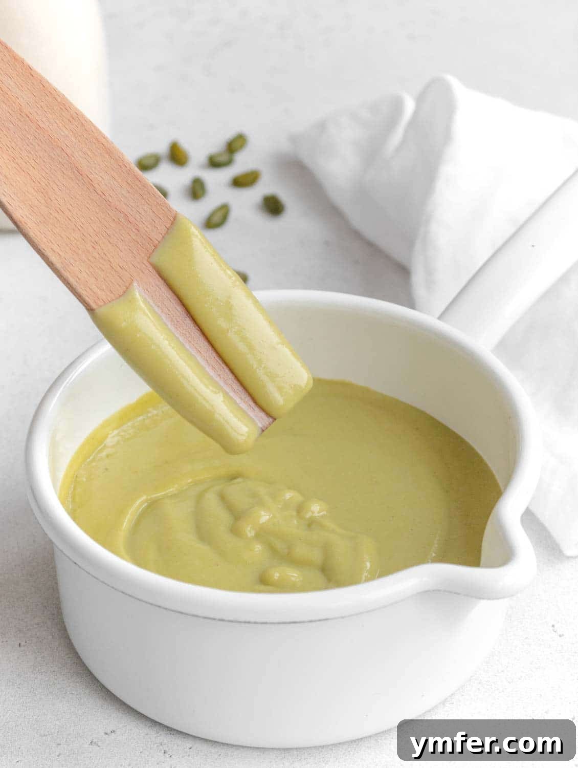 Velvet Pistachio Crème 4 A spoon scooping creamy pistachio custard from a bowl, demonstrating its rich, thick texture.