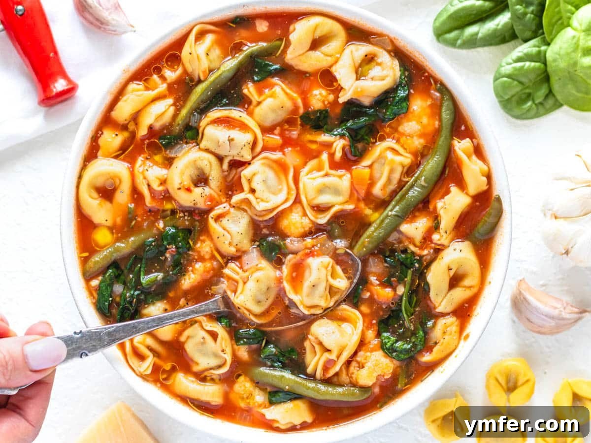 30 Dutch Oven Feasts 12 tortellini soup with spinach and hand holding a silver spoon