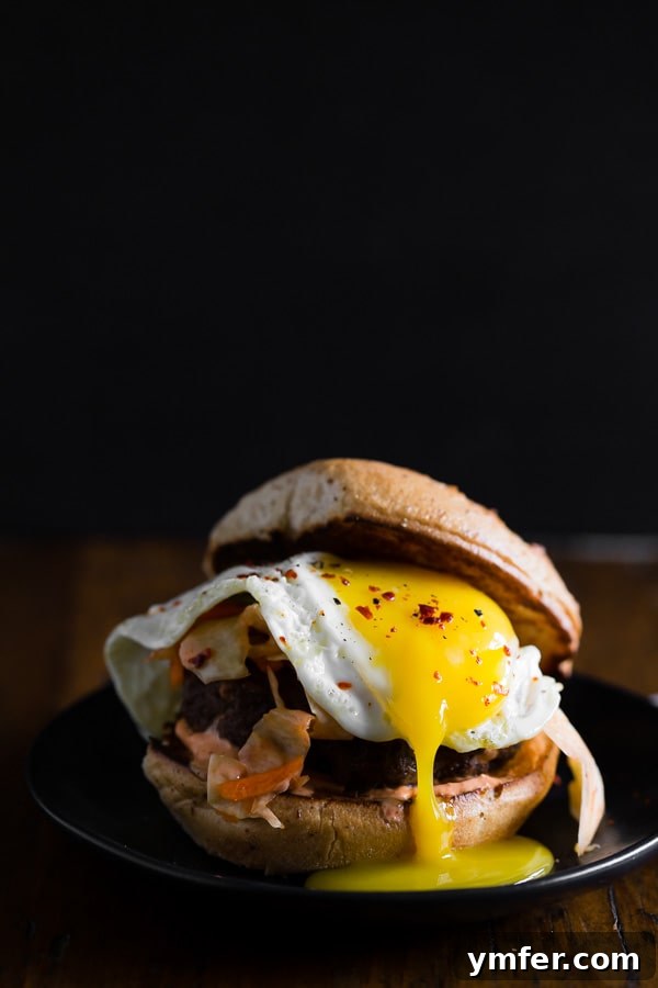 Kimchi Crunch Burger 3 A close-up of a Kimchi Burger showing the gooey melted cheddar cheese, the soft gluten-free bun, and the rich textures of the fried egg and kimchi.