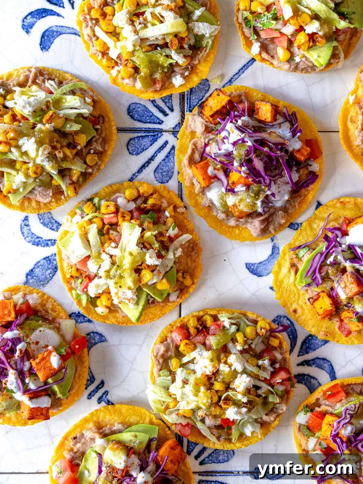 Crispy Topped Tortilla Delights 2 Vibrant tostadas featuring refried beans, roasted sweet potato, avocado, and sour cream, arranged on blue tiles.