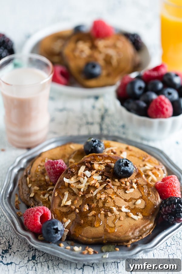 Golden Coconut Espresso Griddlecakes 2 Fluffy Toasted Coconut Espresso Pancakes stacked high, topped with fresh berries and a drizzle of Truvia Nectar, showcasing their appealing golden-brown texture.