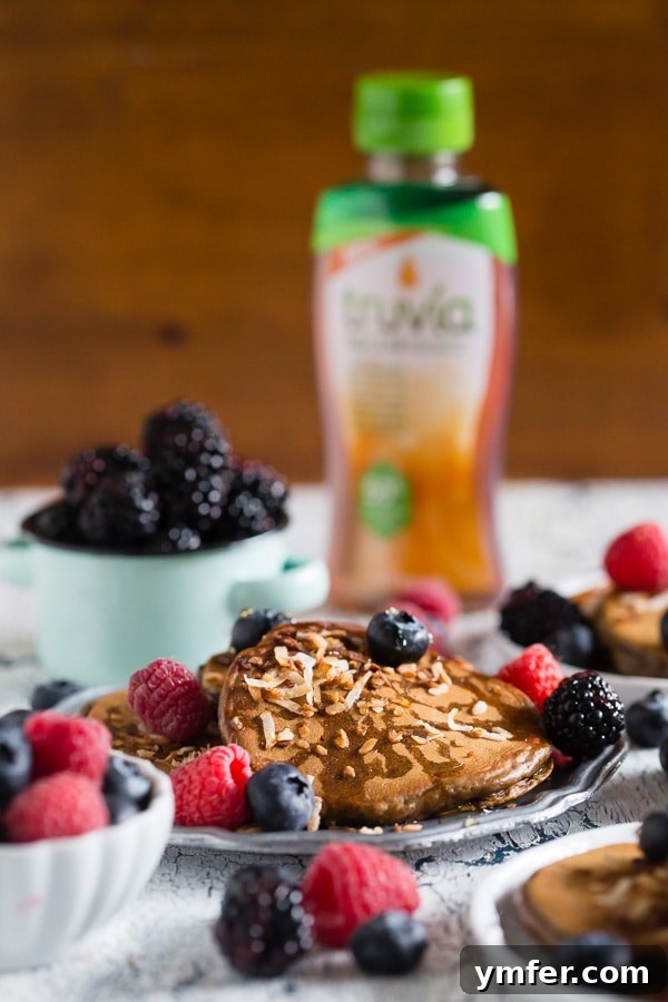 Golden Coconut Espresso Griddlecakes 4 A generous stack of Toasted Coconut Espresso Pancakes, artistically arranged with fresh raspberries, blueberries, a dusting of toasted coconut, and a glistening drizzle of Truvia Nectar.