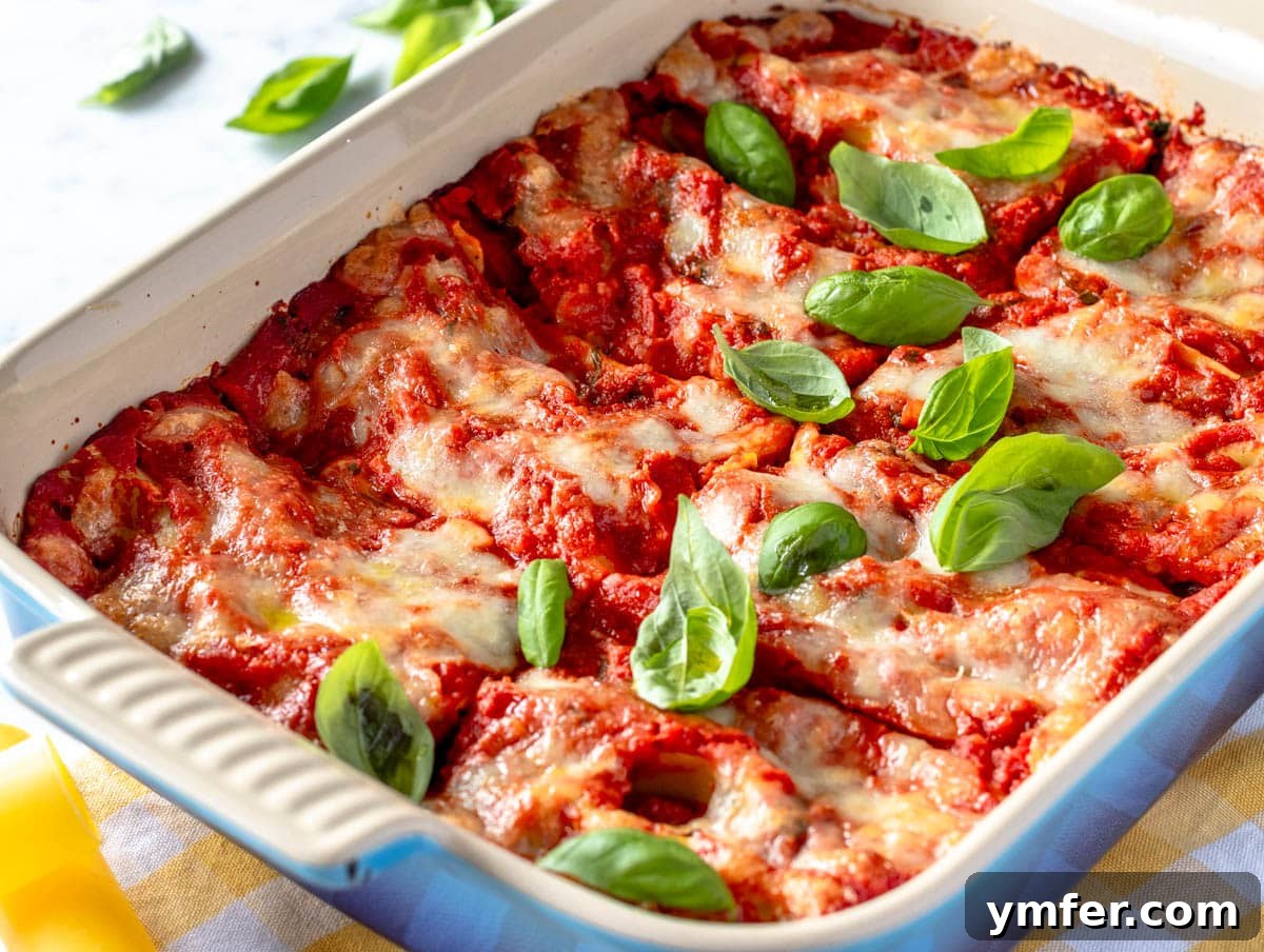 Hearty Stuffed Pasta Bake 12 A close-up shot of baked cannelloni in a blue baking dish, topped with melted cheese and fresh basil.
