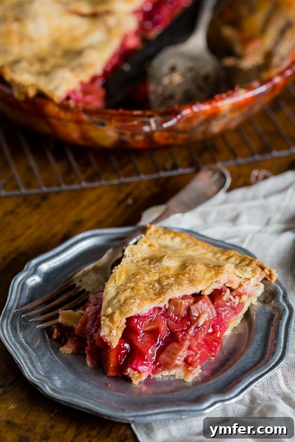 A close-up of a slice of strawberry rhubarb pie on a ceramic plate, showing the juicy filling and golden crust.