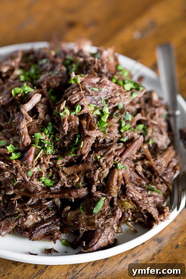The Ultimate Homemade Mississippi Pot Roast 2 Homemade Mississippi Pot Roast shredded and served on a plate, garnished with fresh herbs and bell peppers.