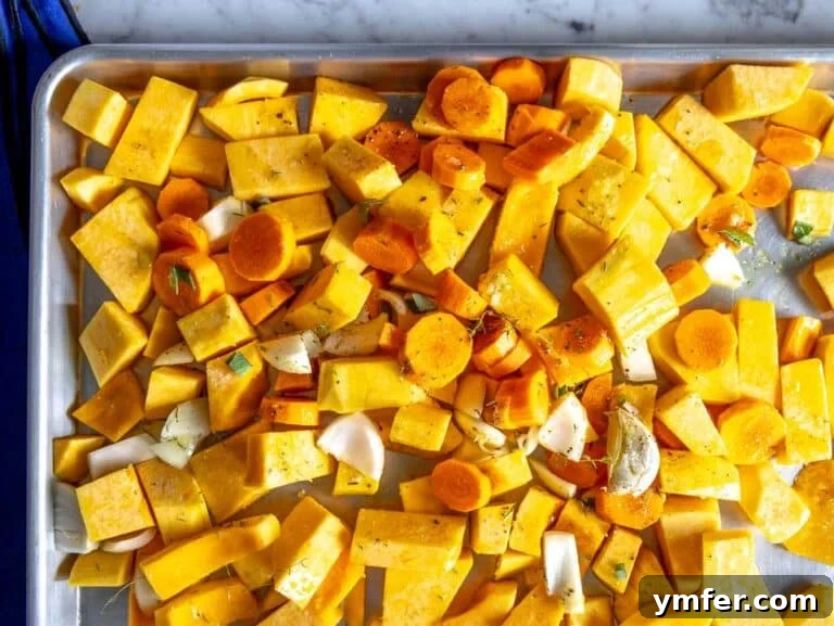 Chopped butternut squash, carrots, onion, garlic, thyme, and sage on a baking tray, ready for roasting.