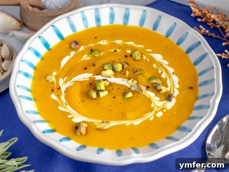 Butternut squash soup topped with toasted nuts, a swirl of cream, and fresh herbs in a bowl.