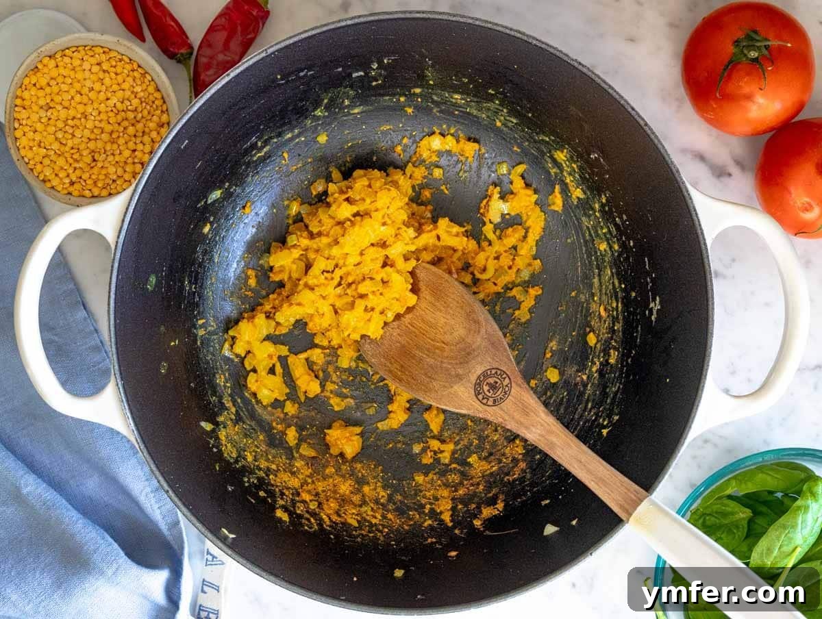 The aromatic flavor base for dal, showing sautéed onions, ginger, garlic, and spices cooking in a pot, filling the kitchen with rich aromas.