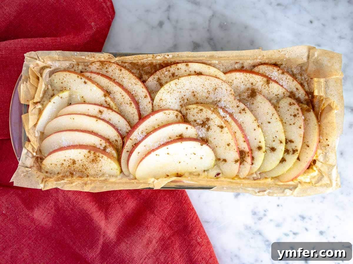 The apple bread batter in the loaf pan, topped with apple slices, ready for baking.
