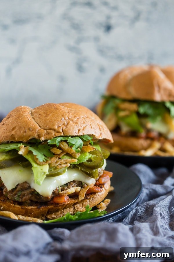 Two Baja burgers presented on a rustic wooden table, with one in the foreground showcasing its rich toppings, and another blurred in the background.