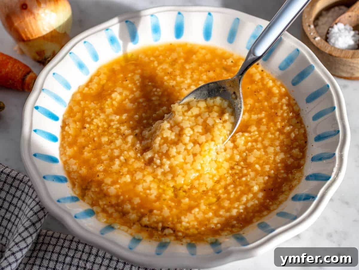 Soothing Small Pasta 7 A bowl of creamy Pastina with grated Parmesan cheese, olive oil, and a blue spoon.