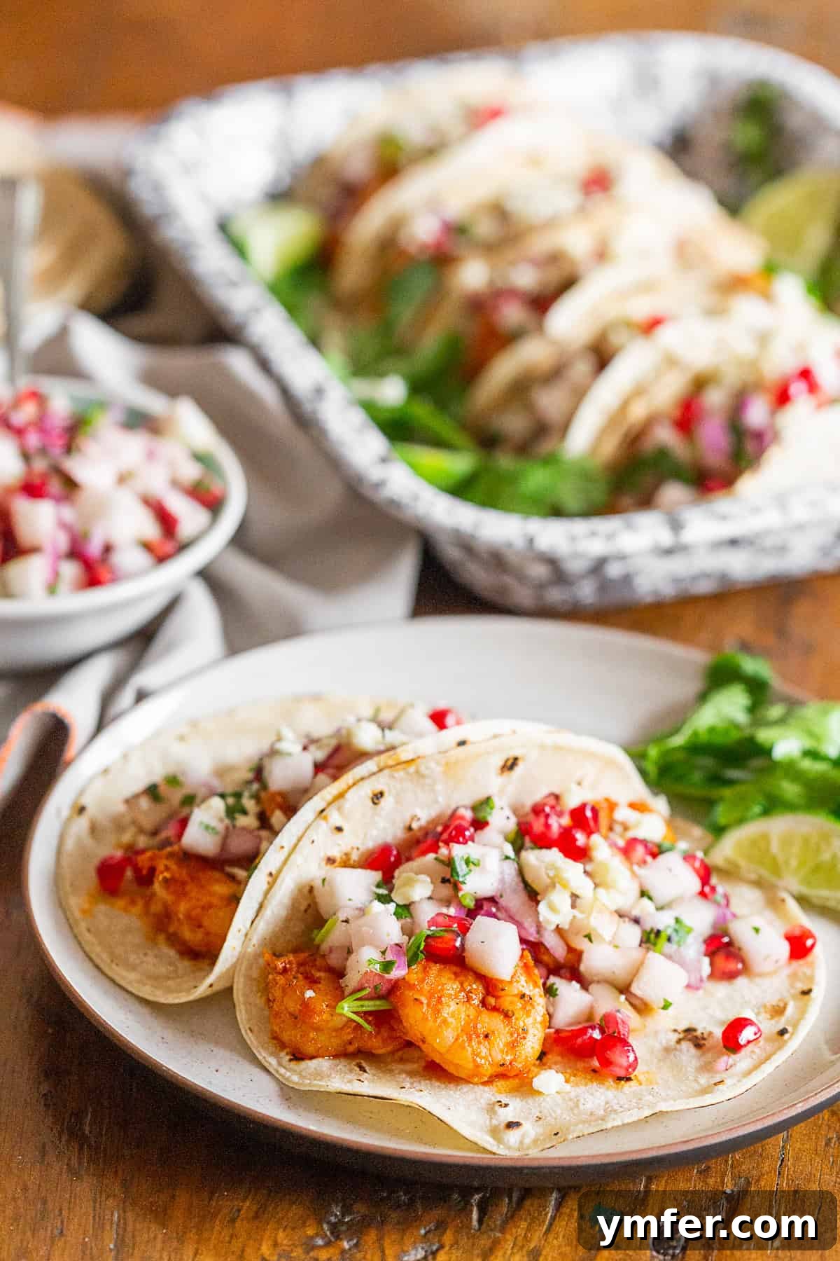 Gourmet Shrimp Tacos with Bright Apple Pomegranate Salsa 2 Vibrant shrimp tacos arranged neatly on a plate, generously topped with a colorful apple and pomegranate salsa.