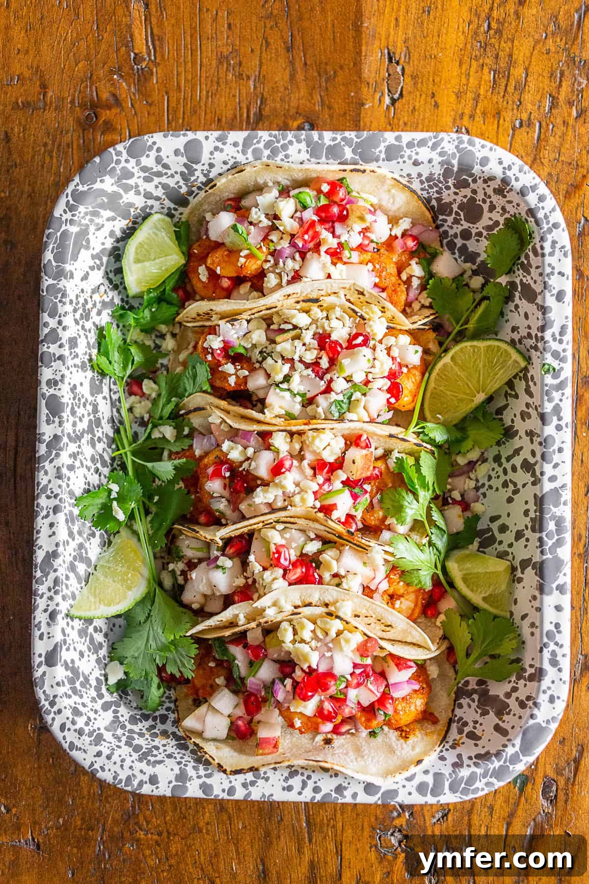 Gourmet Shrimp Tacos with Bright Apple Pomegranate Salsa 3 A close-up view of multiple shrimp tacos, piled high with spicy Cajun shrimp and a bright apple pomegranate salsa, ready for serving in a dish.