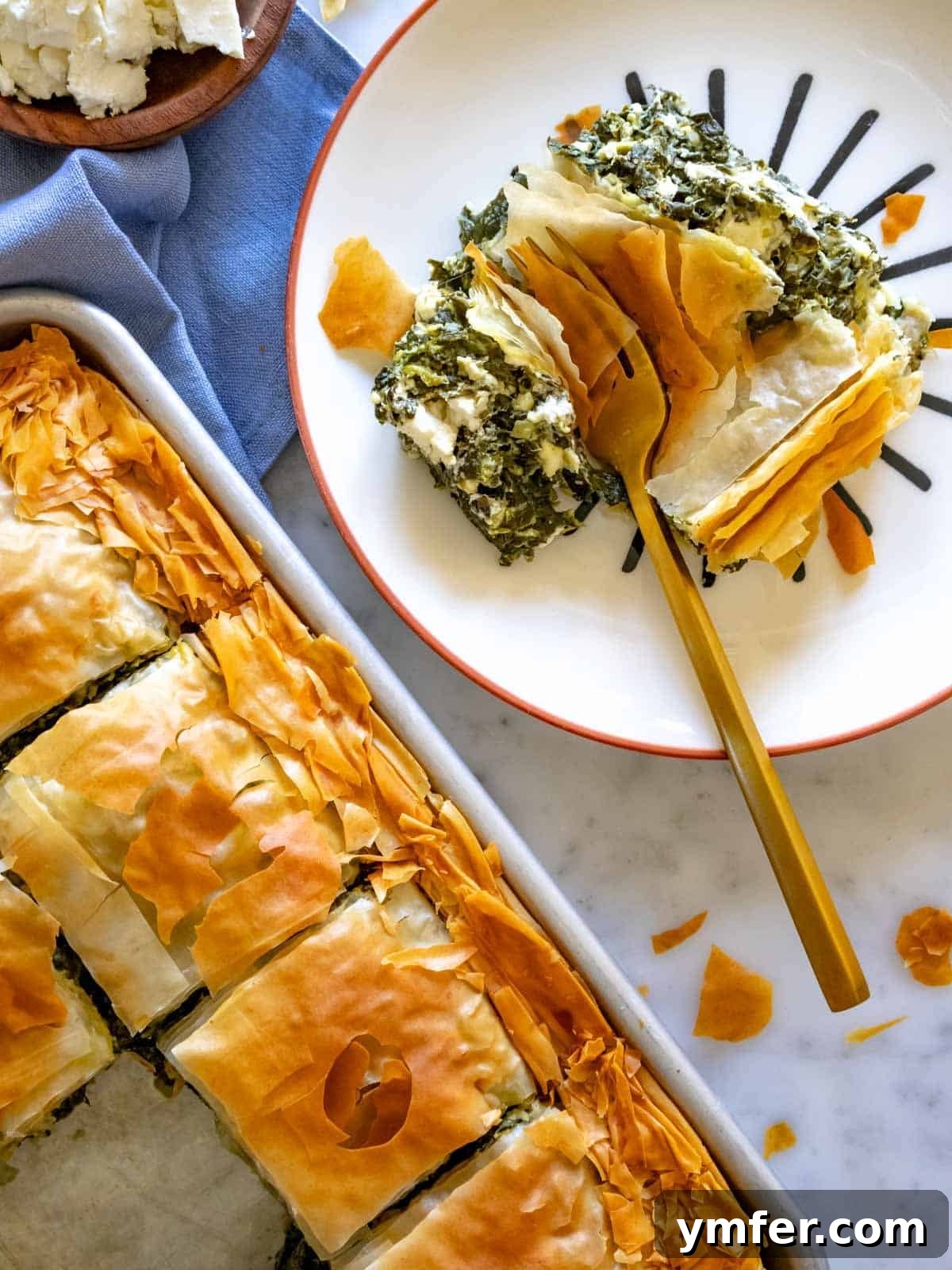 Flaky Greek Spinach and Feta Pie 3 A perfectly golden slice of Greek Spanakopita with its rich spinach and feta filling, presented beautifully on a white plate.