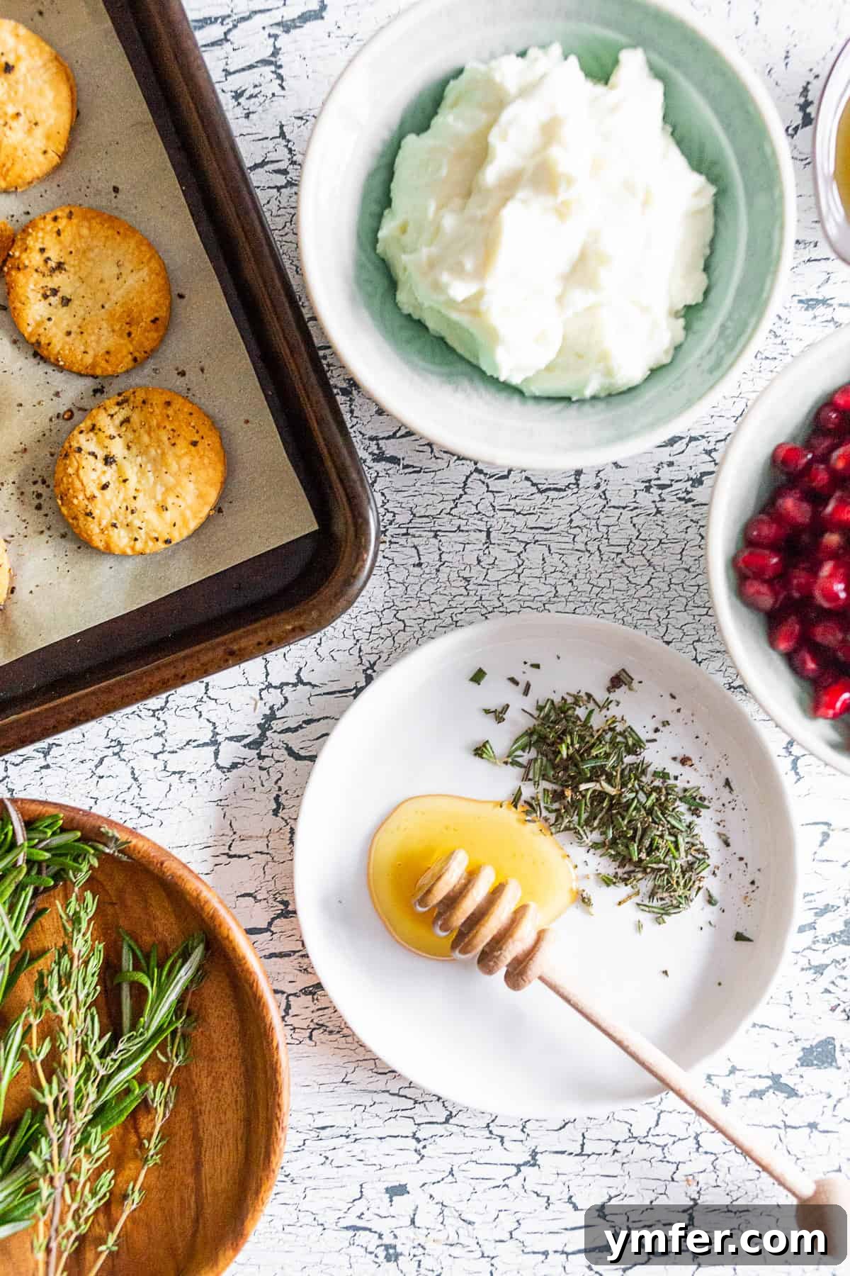 Tangy Chevre Clouds 3 Ingredients for Whipped Goat Cheese Bites on a wooden table: pie crust cracker, whipped goat cheese, honey, rosemary, and pomegranate seeds.