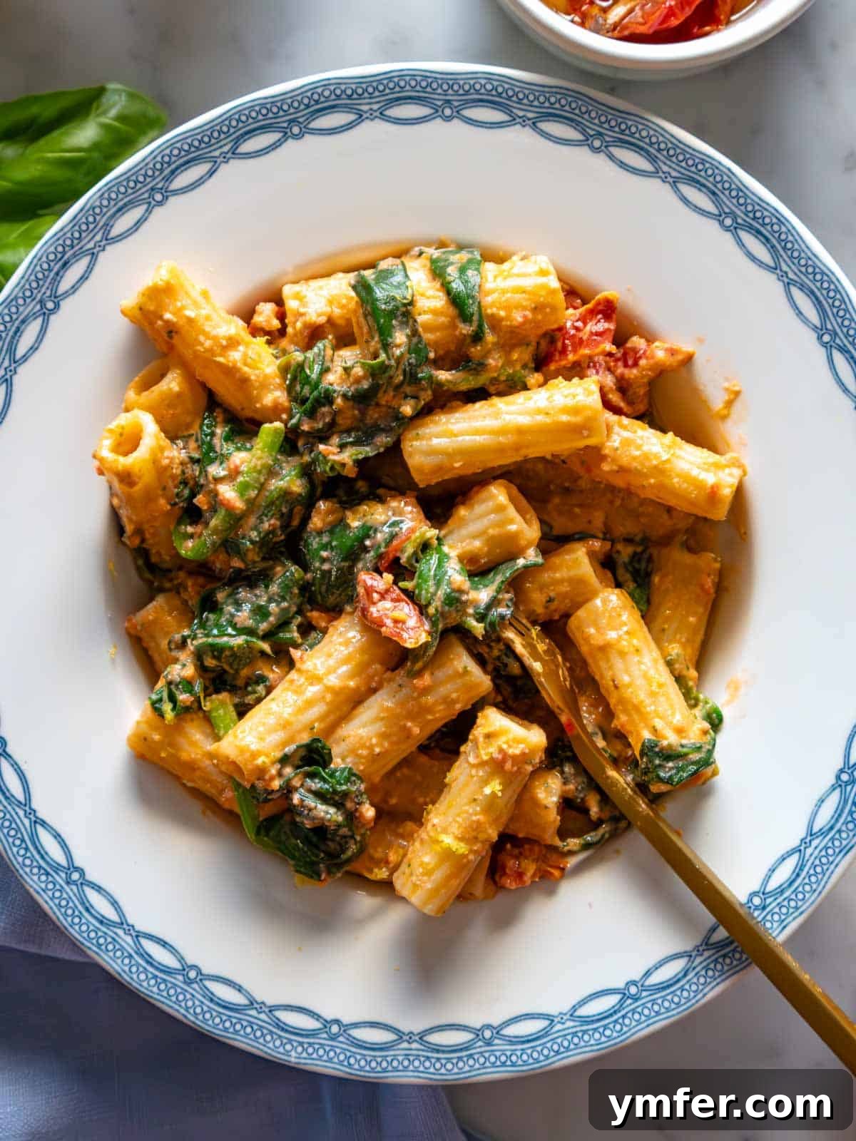 Sun-Kissed Tomato Pasta 2 Sun-dried tomato pasta with spinach on a blue plate, garnished with fresh basil.