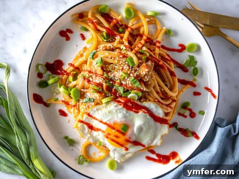 Umami Gold 11 Miso pasta with sriracha sauce, a fried egg, and green onions, ready to eat.