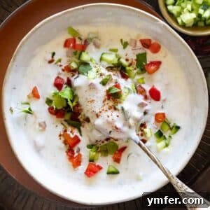Raita in a bowl garnished with ground cumin and cilantro.