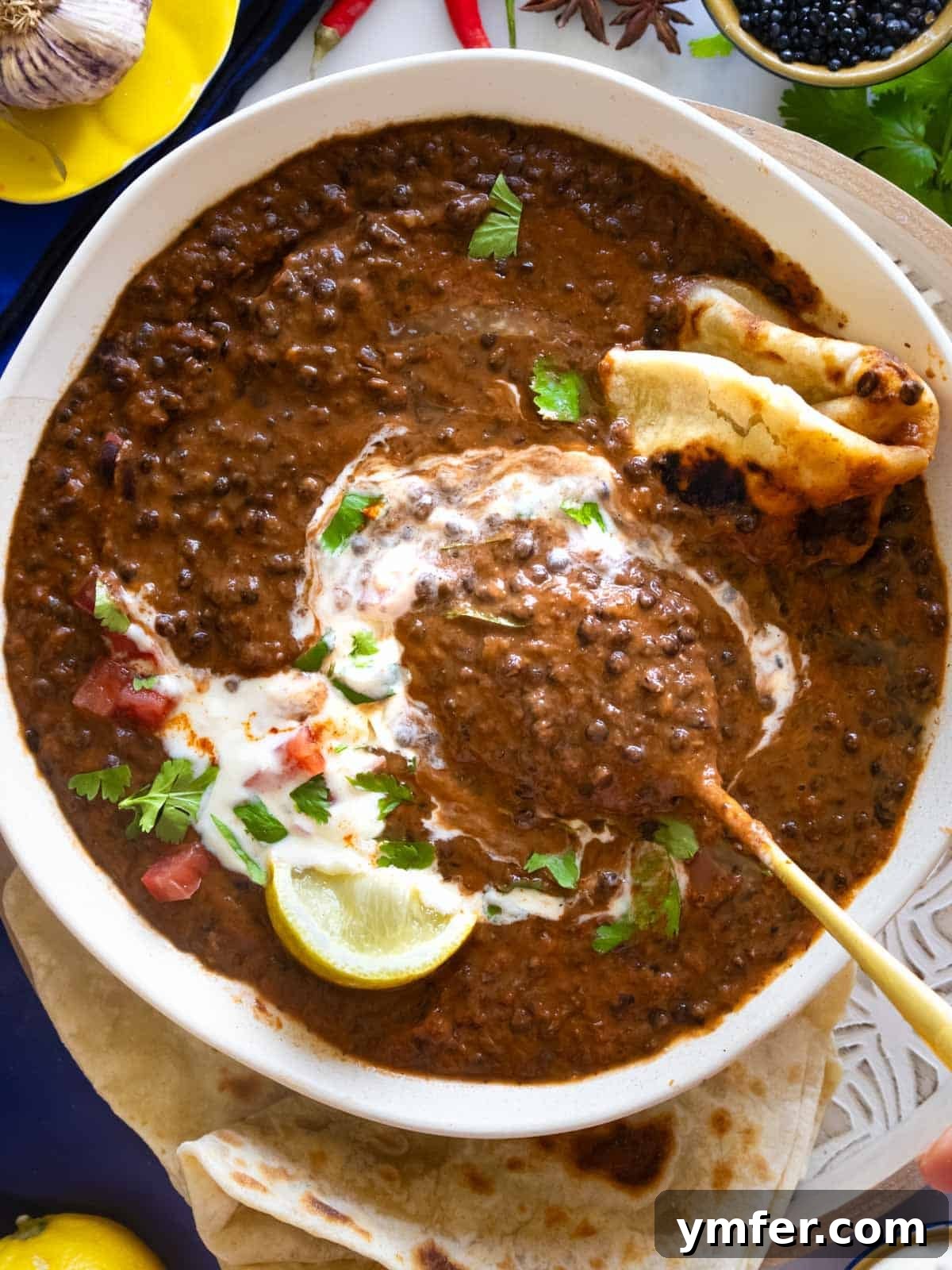 Dal Makhani Black Lentil Curry 3 A bowl of creamy black lentil Dal Makhani, garnished with fresh cream and cilantro, served with a side of paratha bread.