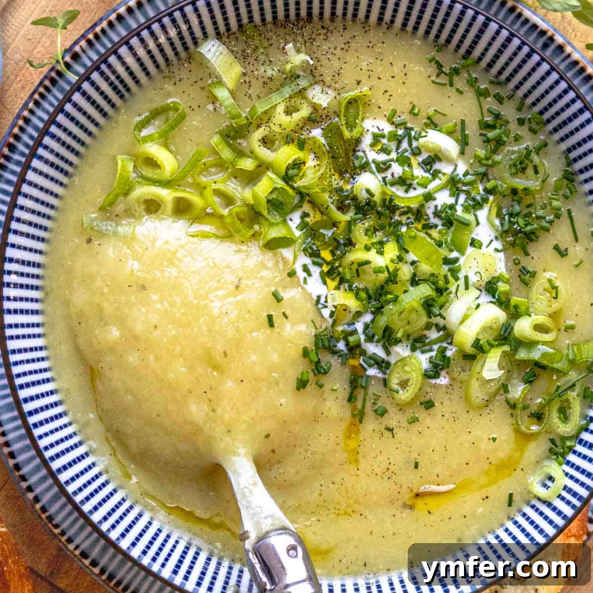 High Satisfaction Low-Calorie Meals 13 A comforting bowl of potato leek soup garnished with fresh chives, next to a spoon.