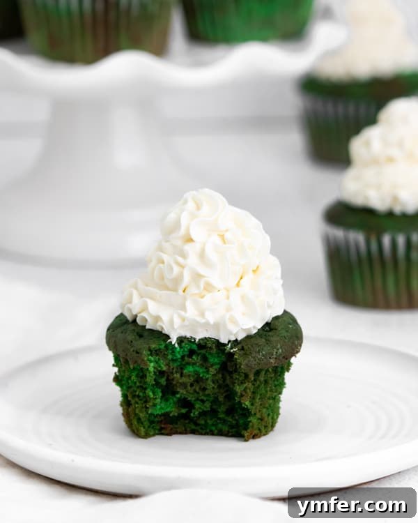 Emerald Velvet Cupcakes 5 Green velvet cupcake with a bite taken out of it, revealing its vibrant interior and fluffy frosting.