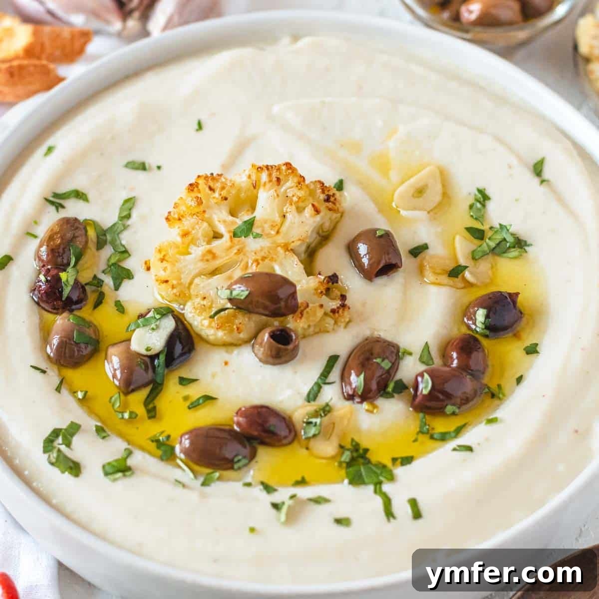 A bowl of creamy cauliflower soup, garnished with olives and freshly chopped parsley.