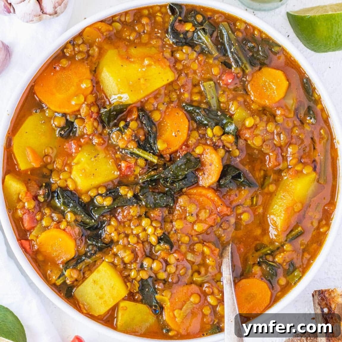 Hearty curry lentil soup with tender carrots, kale, and potatoes, garnished with fresh herbs.