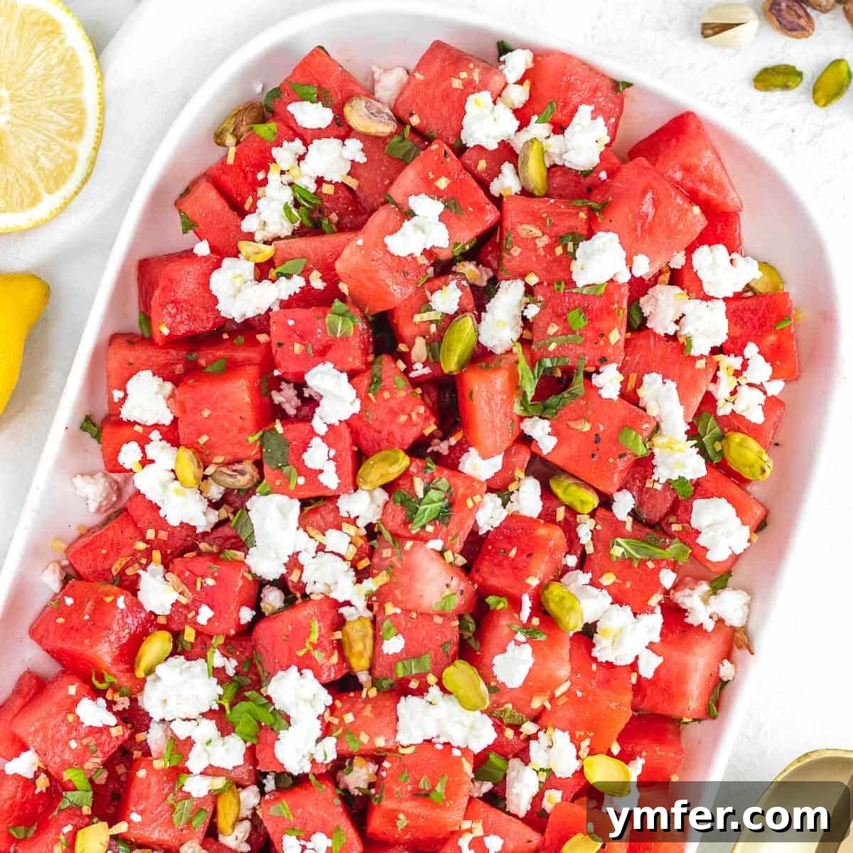 A vibrant watermelon salad arranged on a serving platter, garnished with fresh mint and crumbled feta cheese.