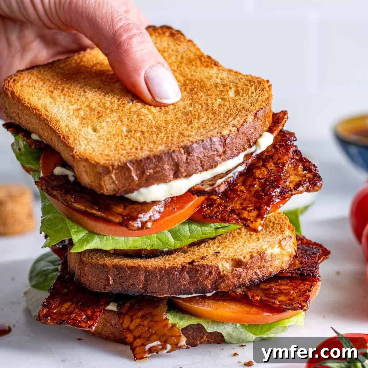 Heart-Smart Meals 26 Tempeh bacon in a BLT sandwich and a hand. A crispy and savory plant-based bacon alternative.
