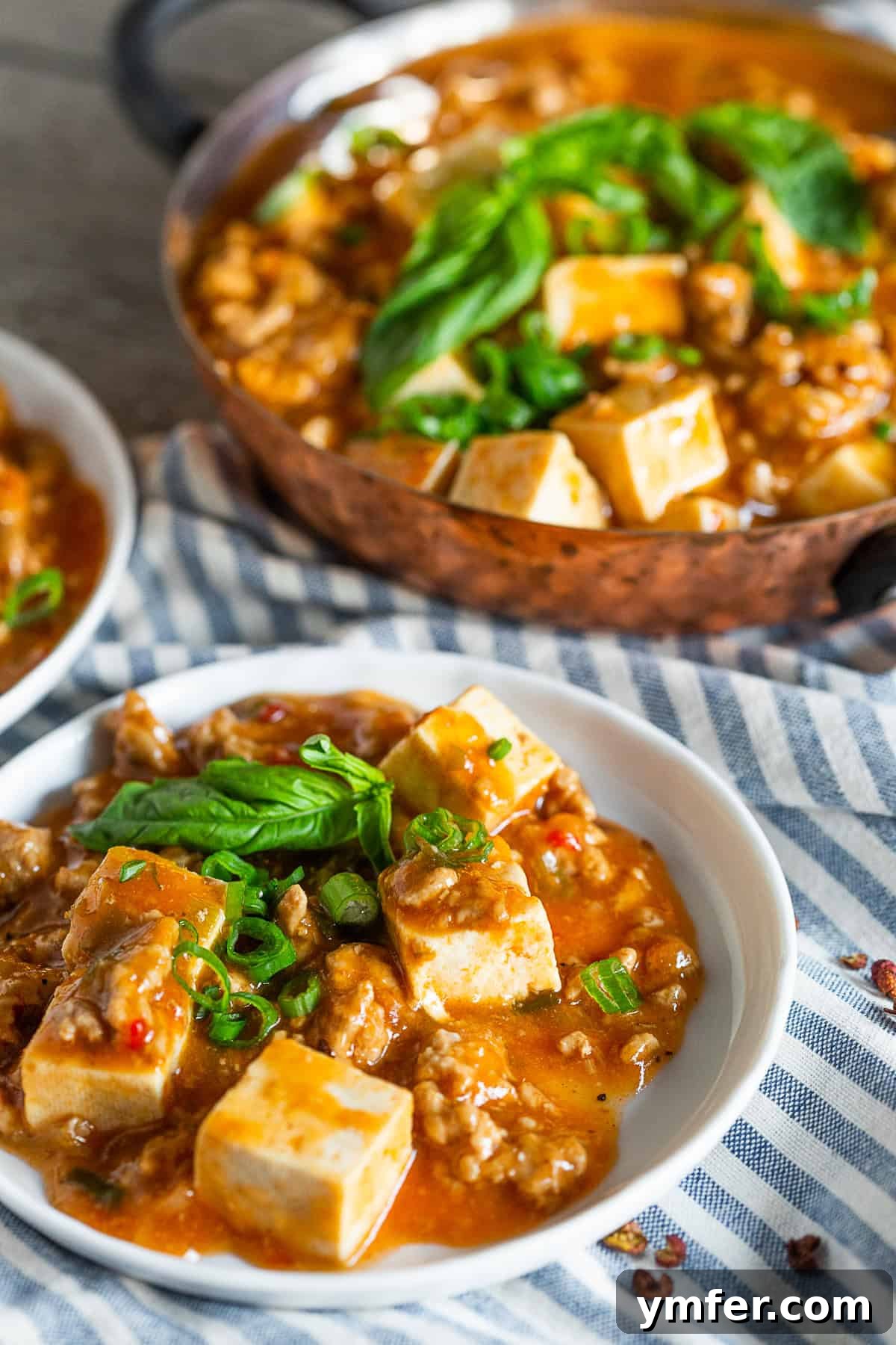 Spicy Minced Pork Mapo Tofu 5 A serving of Ground Pork Mapo Tofu topped with vibrant fresh basil and chopped green onions in a white bowl.