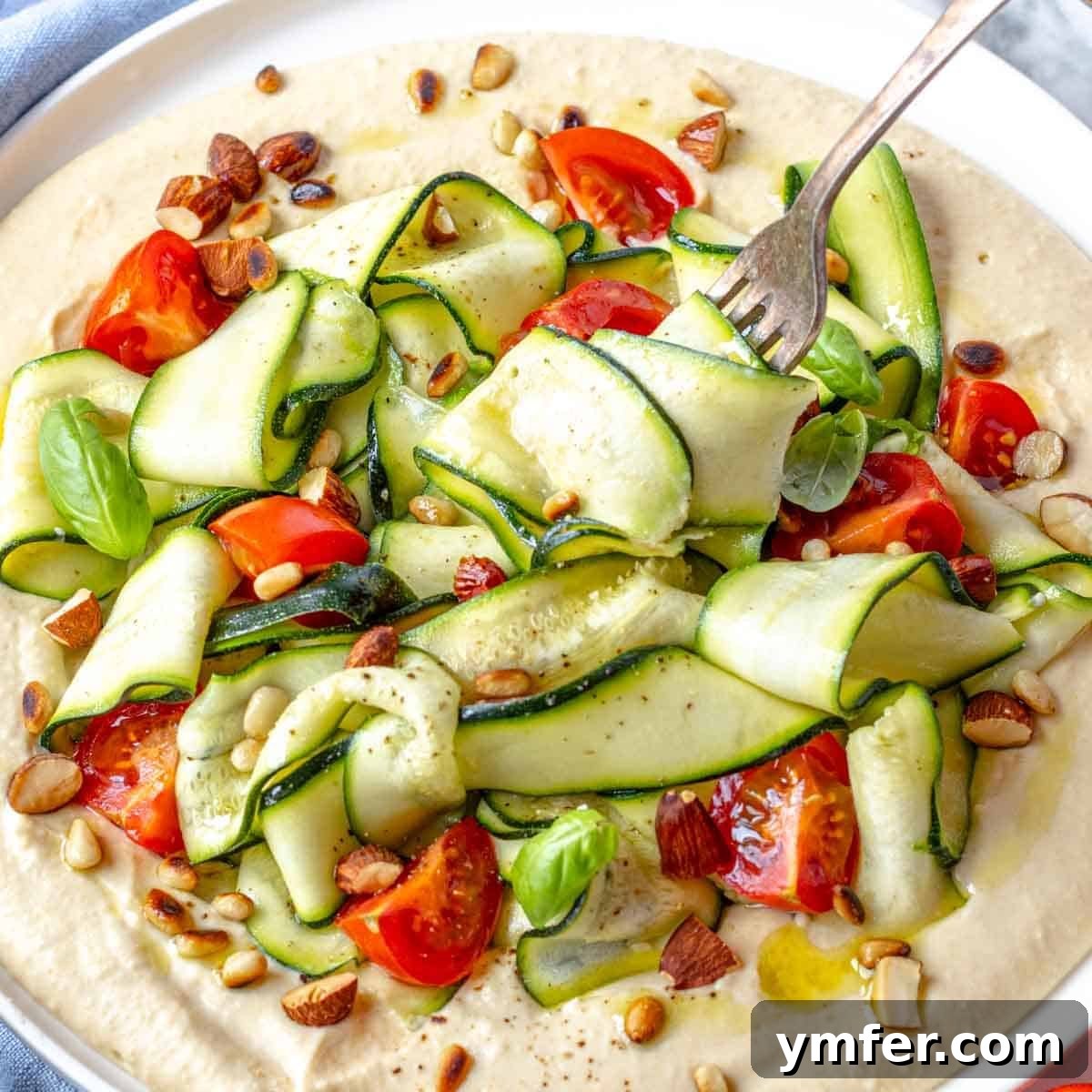21 Fresh & Flavorful Summer Salads 12 Zucchini salad with toasted nuts on hummus served with a fork.