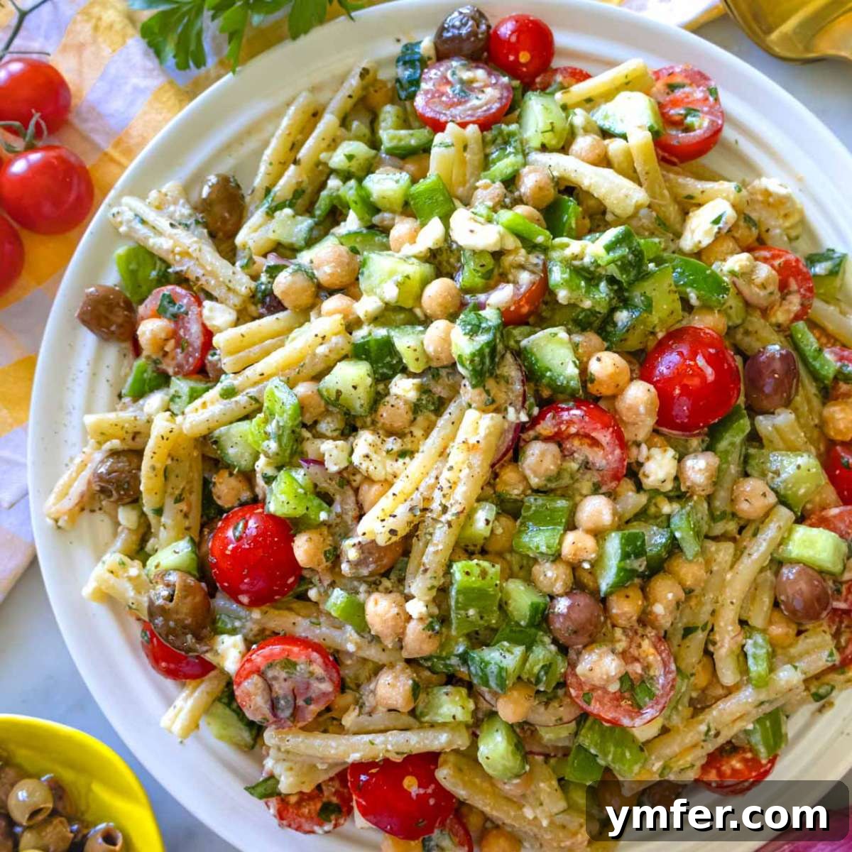 30 Delectable Picnic Recipes 7 A platter of authentic Greek pasta salad featuring feta, olives, cucumber, and tomatoes, garnished with lemon wedges – an easy Mediterranean summer recipe.