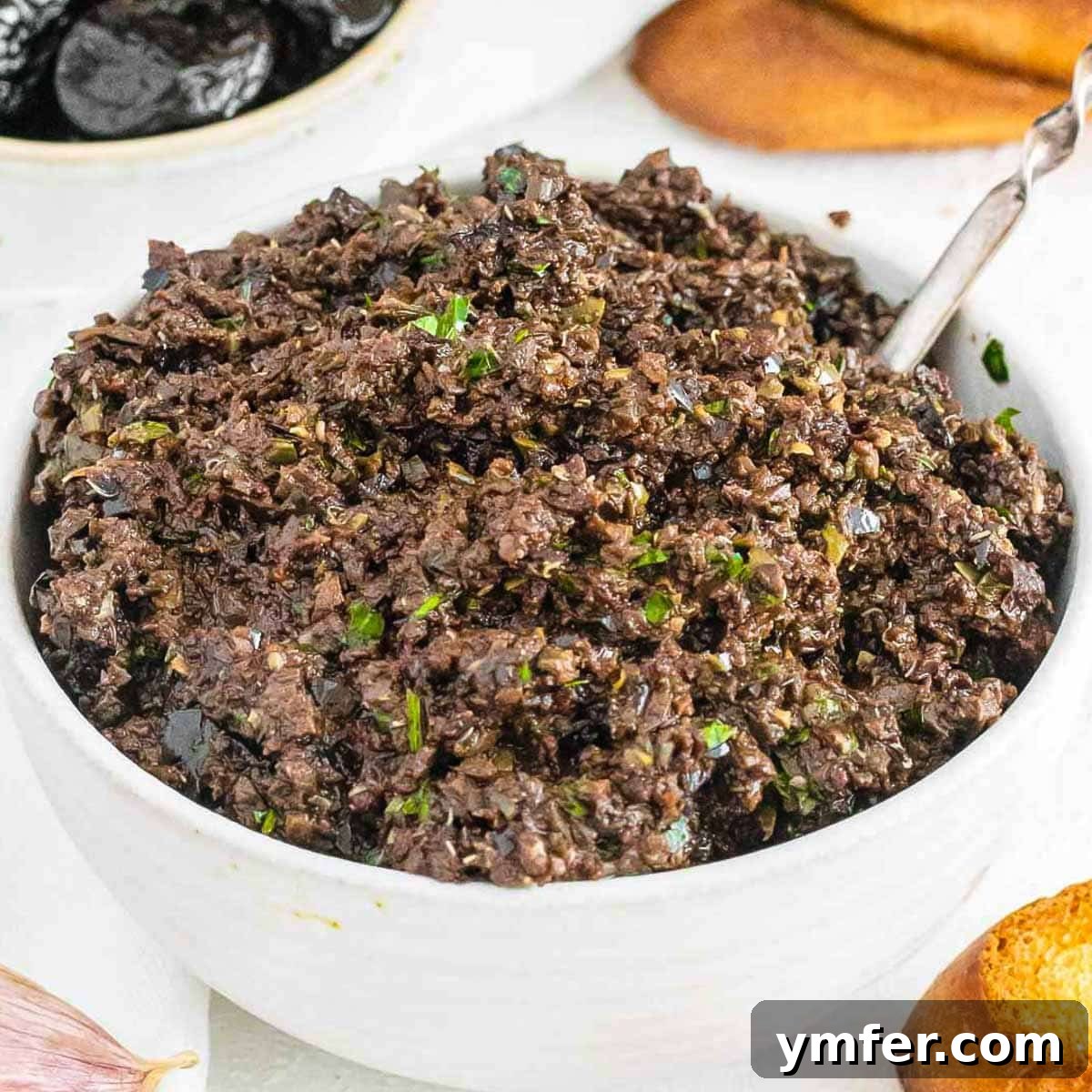 21 Greek Kitchen Classics 6 Dark, rich olive tapenade in a small white bowl, showcasing its texture.