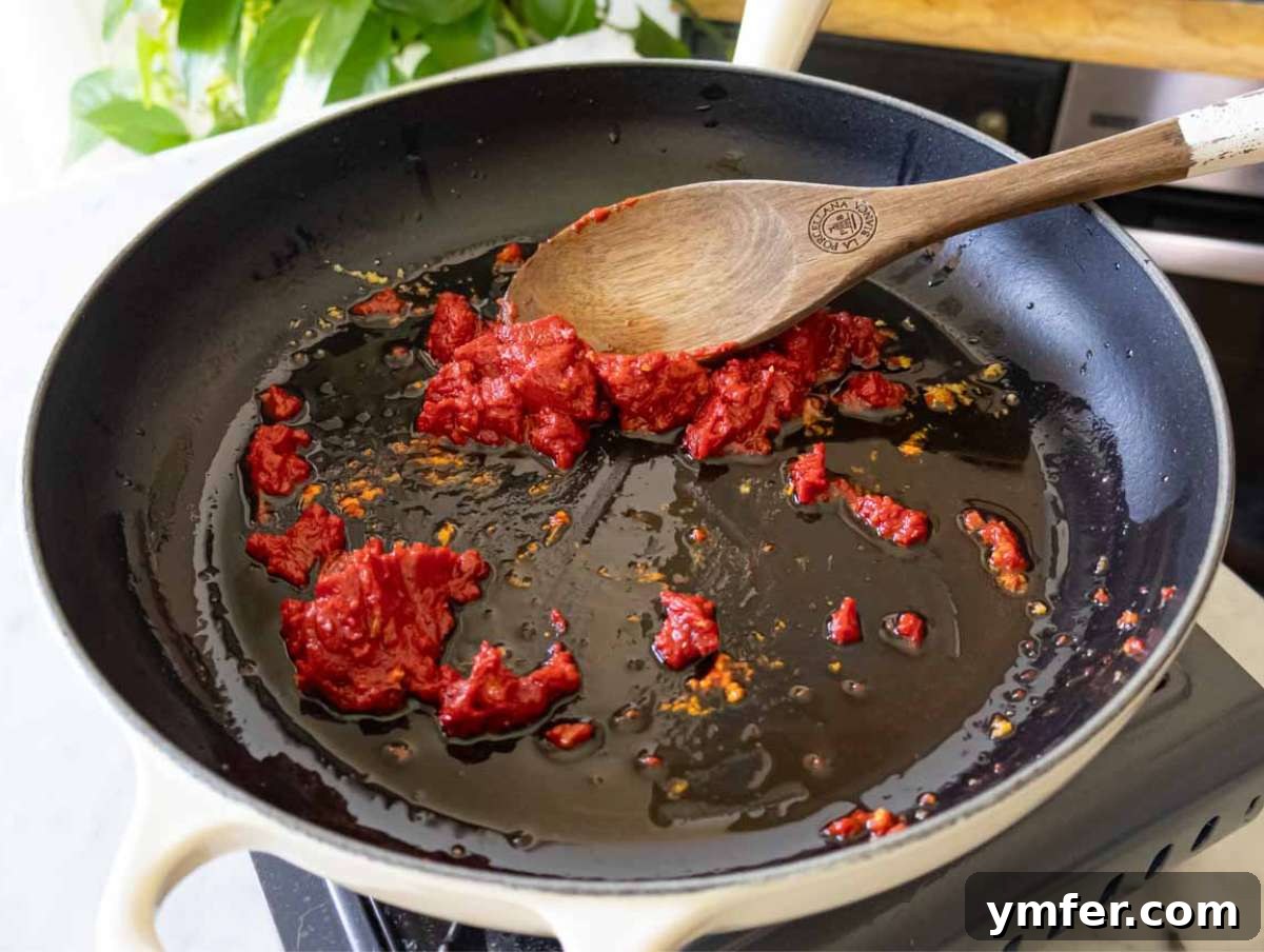 Say Yes To This Orzo 5 Garlic, red pepper flakes, and tomato paste sizzling gently in olive oil within a skillet, creating a fragrant base for the Marry Me Orzo.