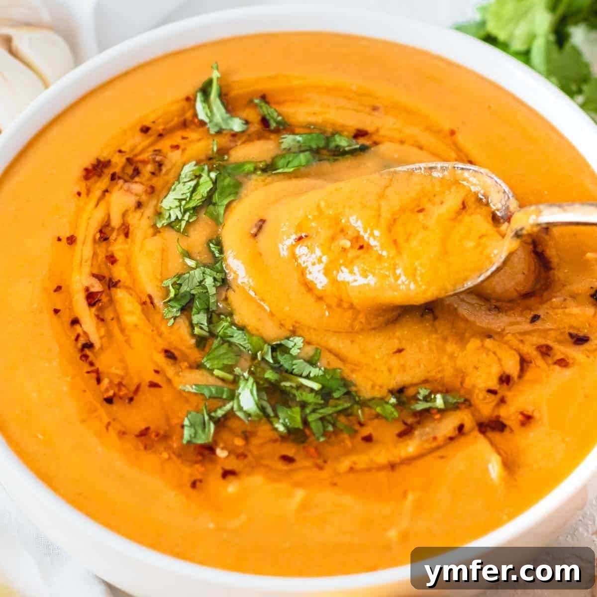 9 Mediterranean Proteins to Power Your Plate 8 Creamy Turkish red lentil soup in a bowl, garnished with a swirl of chili oil and a silver spoon, inviting a taste.