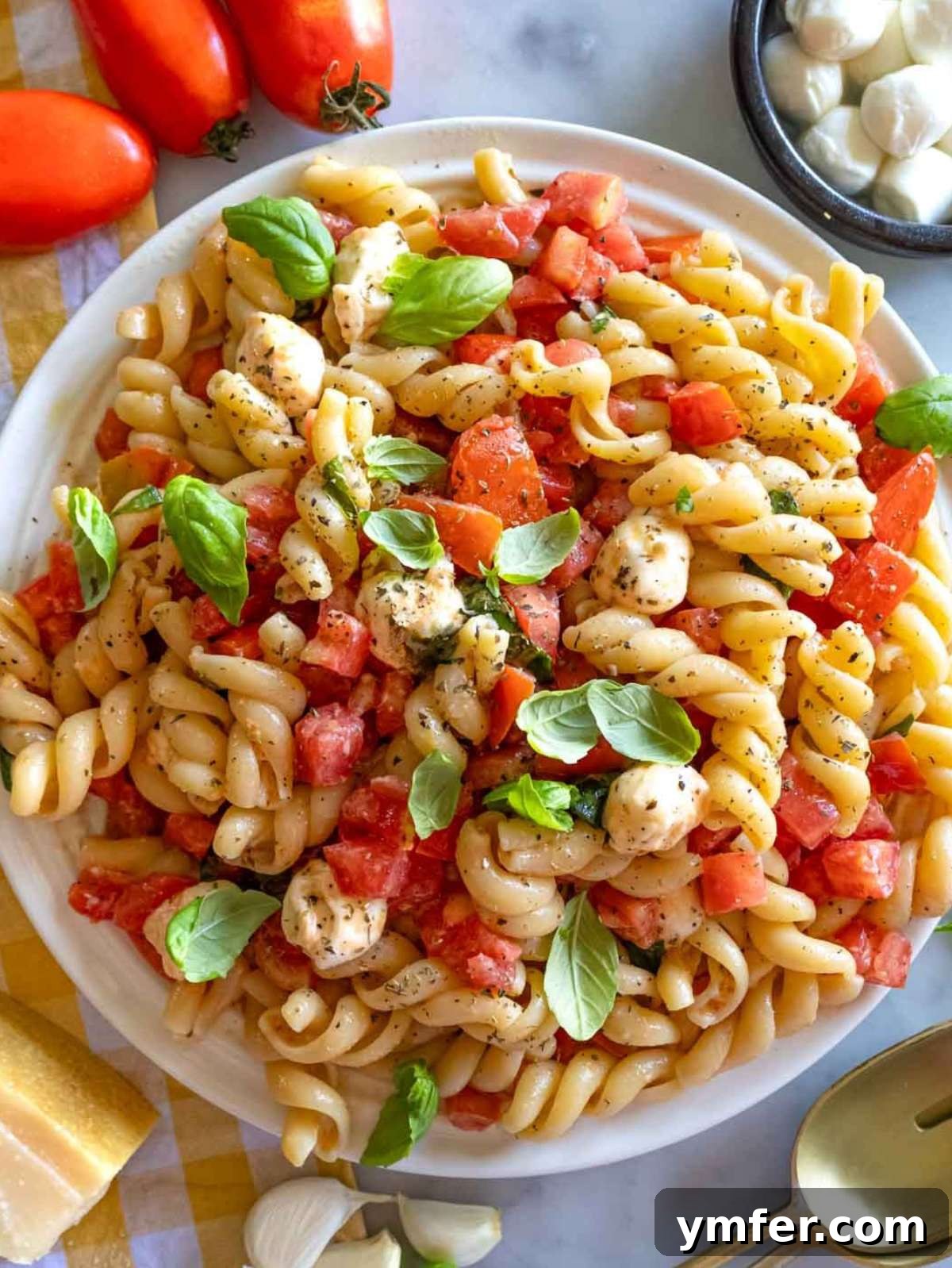 Easy Bruschetta Pasta No Cook Sauce 2 Top-down view of bruschetta pasta with fresh basil, mozzarella, and tomatoes on a rustic table, invitingly garnished.