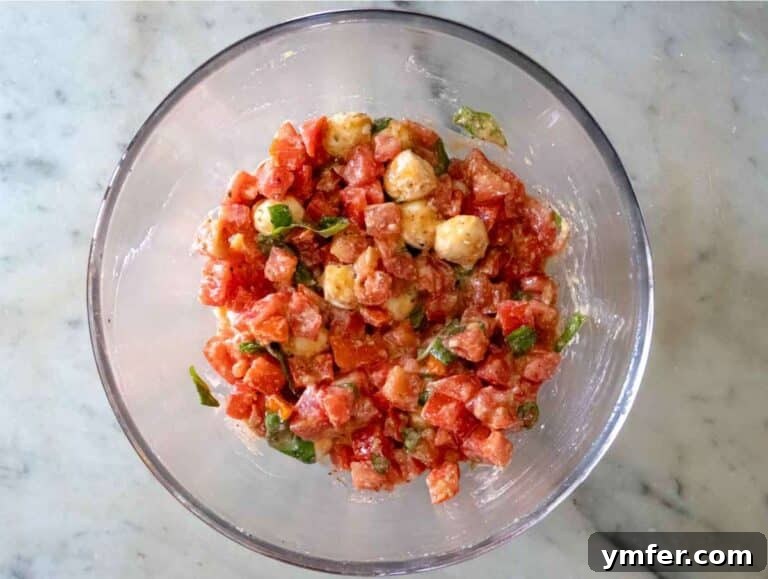 Easy Bruschetta Pasta No Cook Sauce 9 Step 1: Vibrant tomato mixture with fresh basil, grated garlic, rich olive oil, and creamy cheese marinating in a pristine white mixing bowl.
