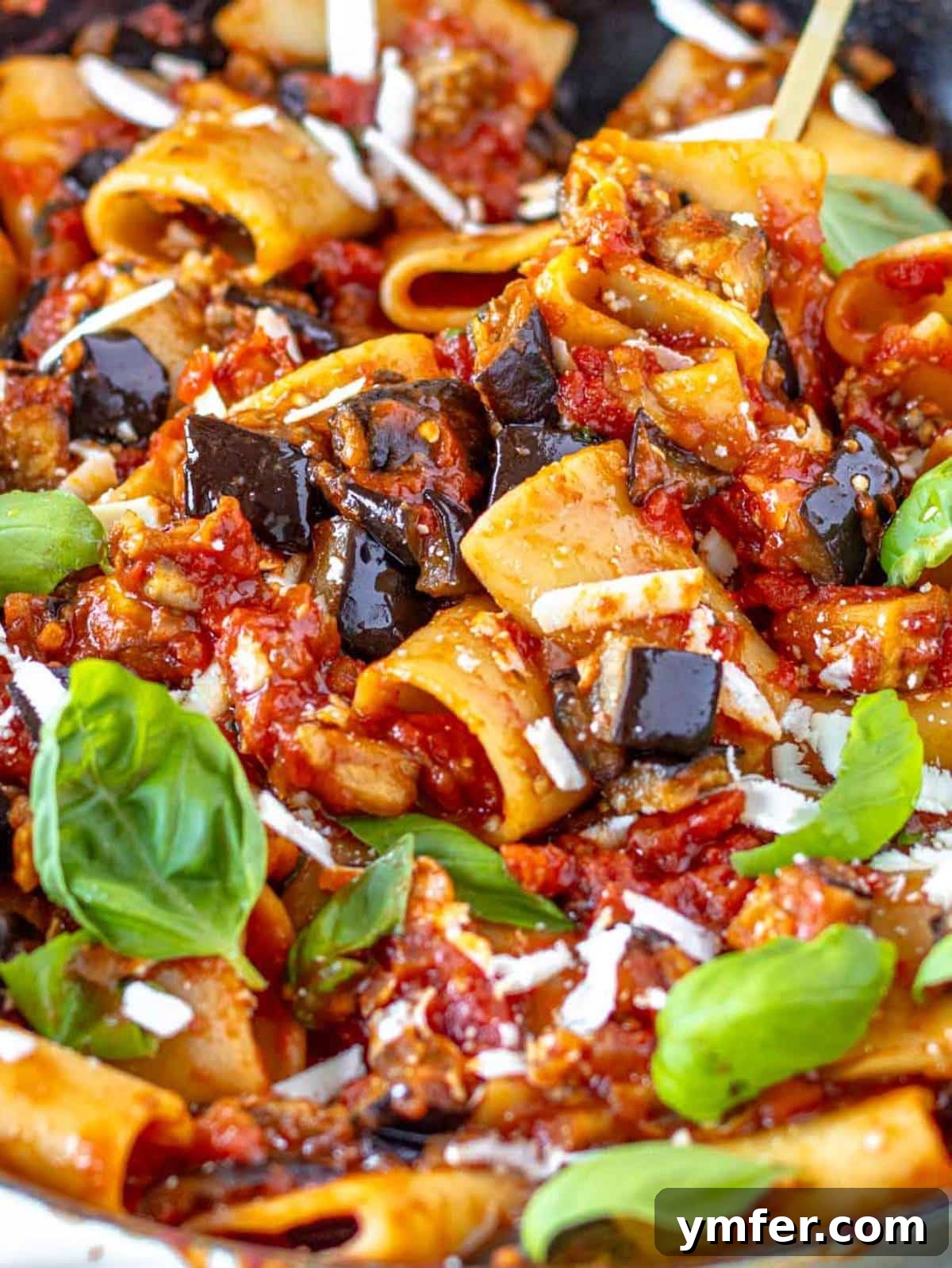 Close up of pasta alla Norma with tender eggplant cubes and fresh basil leaves.