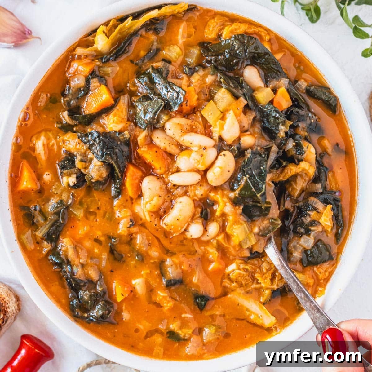 19 Simple Bean Recipes to Slash Your Weekly Food Bill 13 Hearty Tuscan white bean soup, with a hand reaching for a spoonful, suggesting warmth and comfort.