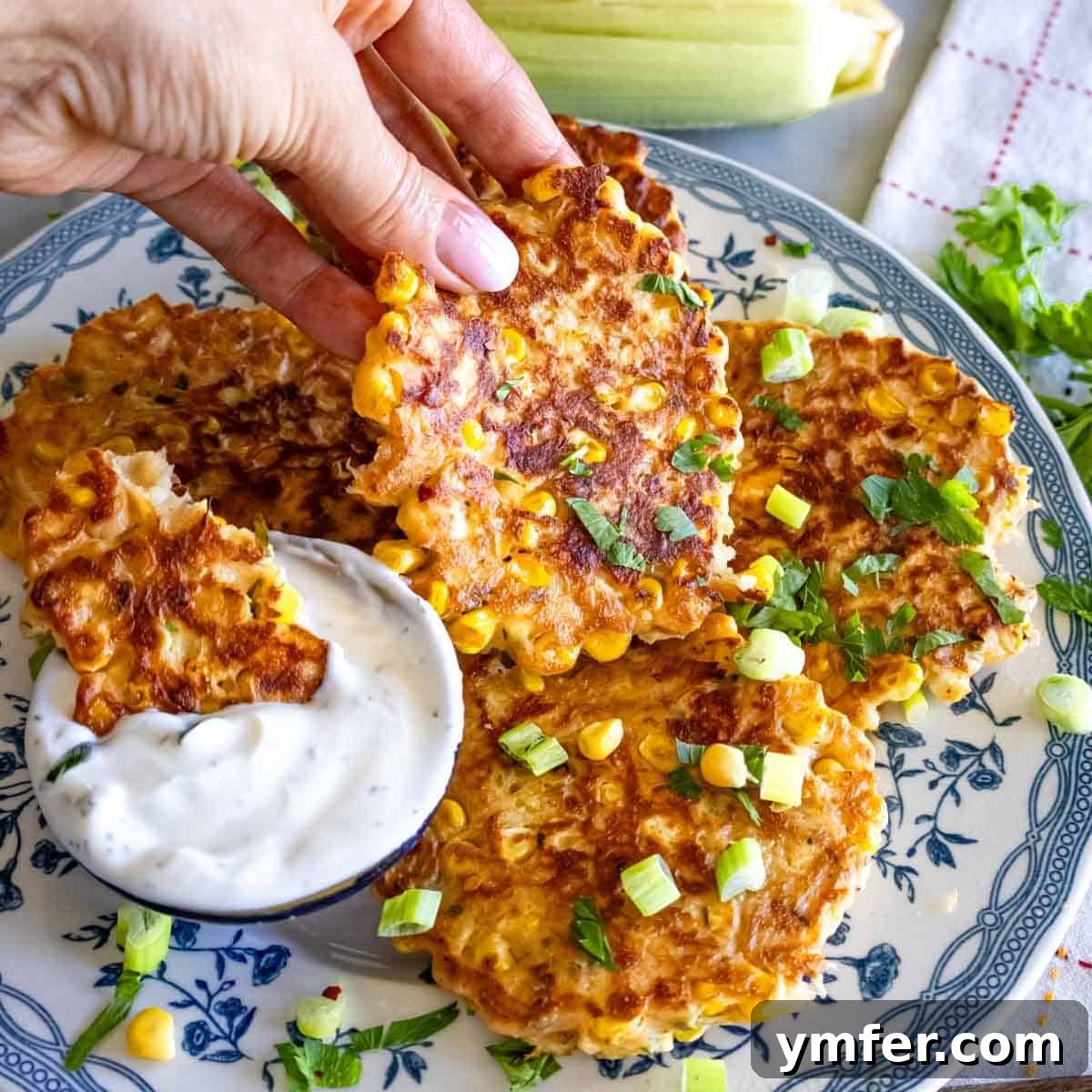 19 Brilliant Greek Yogurt Recipes for Lunch Dinner and Dessert 14 Louise holding a corn fritter while another is dipped in yogurt on a serving plate, showcasing a versatile Greek yogurt recipe.