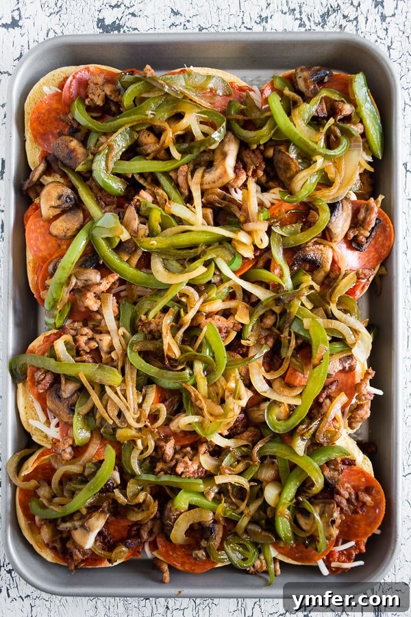 Close-up of Baked Supreme Pizza Sliders, showing the layers of pepperoni, sausage, vegetables, and melted mozzarella cheese piled high on the soft buns.