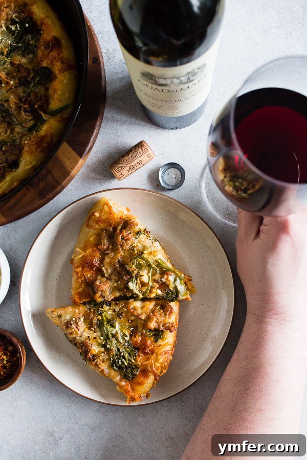 A slice of Sausage Broccoli Rabe Skillet Pizza being served with a glass of red wine, highlighting its artisanal appeal and suitability for a gourmet meal experience.